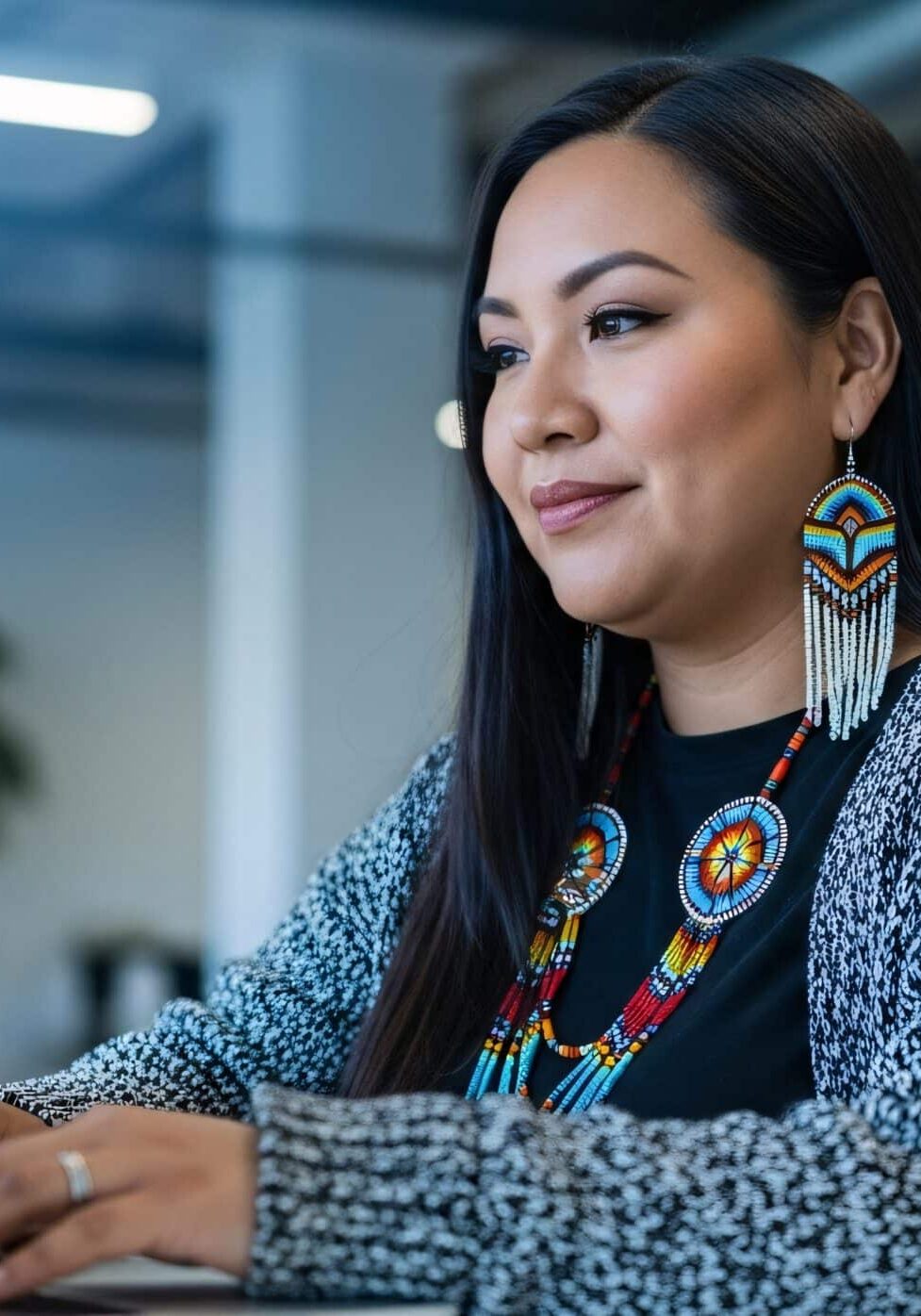 indigenous woman working on laptop in modern office with traditional jewelry